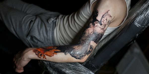 Person showing a detailed tattoo on their arm featuring a female figure and abstract elements.