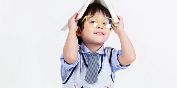 Young boy wearing yellow glasses and holding a book over his head.