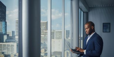 Businessman in a suit working on a laptop by a large office window.