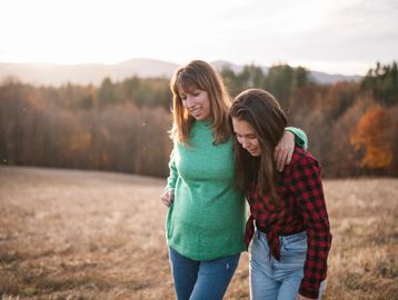 Two women walking arm in arm in a field during autumn.