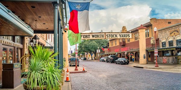 Historic Fort Worth Stockyards street with Texas flag and old brick road.