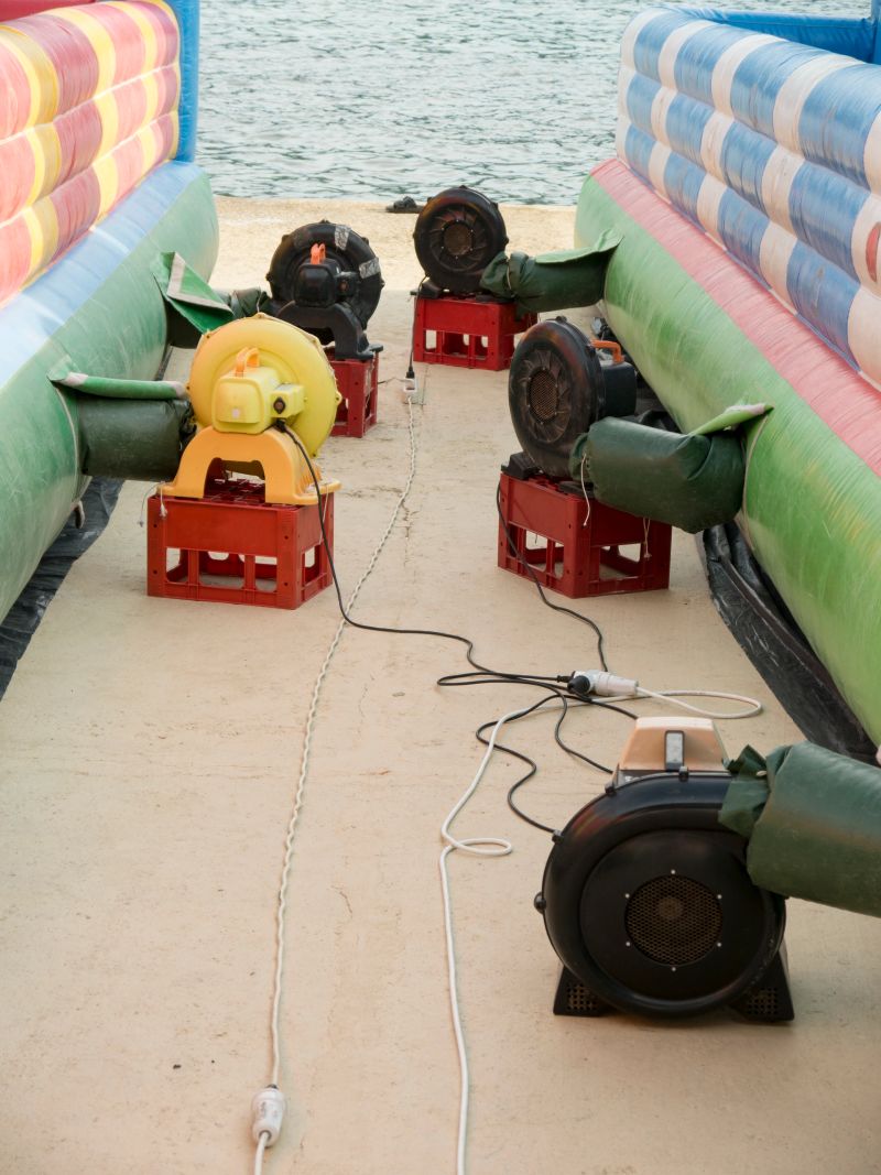 Two giant color fabric trampoline castles laying down on ground inflating with electric air blowers on plastic boxes side view