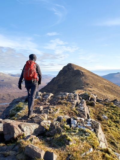 A hiker walks along a rocky mountain ridge under a clear blue sky.