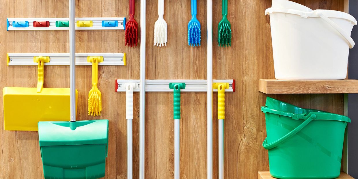 Organized cleaning tools including brushes, dustpans, and buckets on a wooden wall.