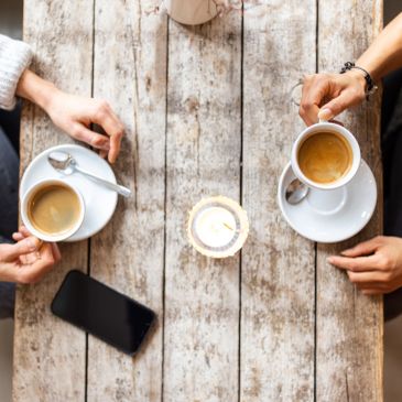 Two people having coffee at a rustic wooden table.