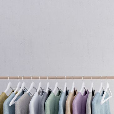 A row of pastel-colored sweaters hanging on white hangers against a plain wall.