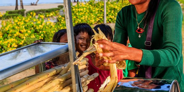 Smiling woman preparing sugarcane juice on a sunny day by the beach.