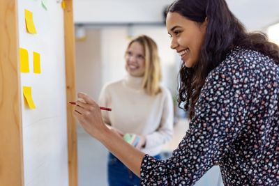 Two women collaborating with sticky notes on a whiteboard.