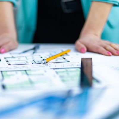 Person reviewing architectural blueprints with a pencil and ruler on the table.