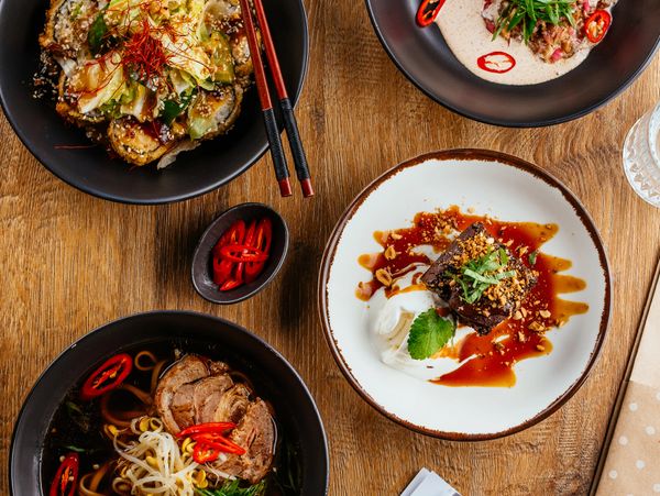 A diverse Asian meal spread featuring sushi, ramen, a savory dish, and a dessert on a wooden table.