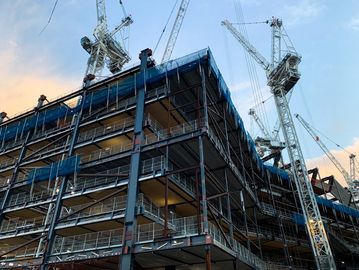Steel scaffolding and cranes at a construction site during sunset.