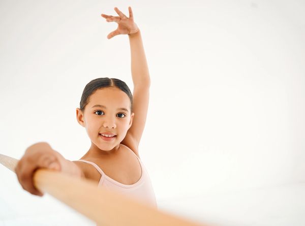 Young girl practicing ballet at the barre with a bright smile.