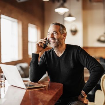 Man talking on phone at a table with laptop.