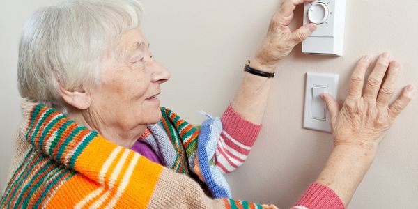 Woman standing by the thermostat and is regulating the cold temperature.