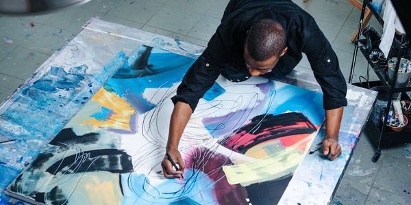 Artist working on a colorful abstract painting on the floor.