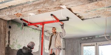 Two workers installing drywall on a ceiling during renovation.