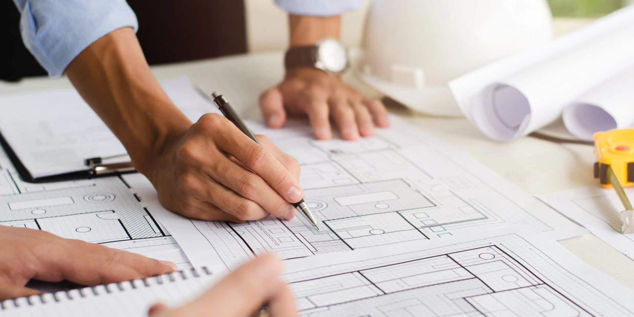 Hands working on architectural blueprints.