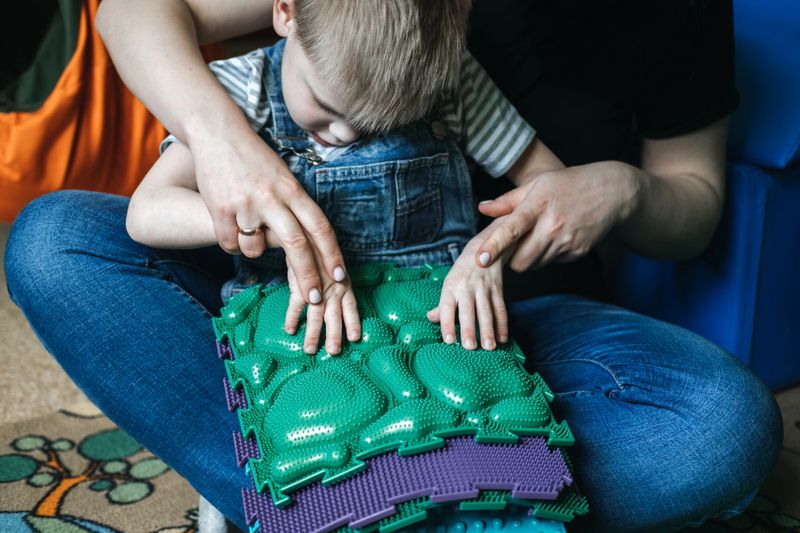 Sensory Play for Kids with Special Needs. Activities for kids with disabilities, Cerebral Palsy. Boy with Cerebral Palsy playing with Sensory Mat Massage Game Puzzle Mats for Kids.
