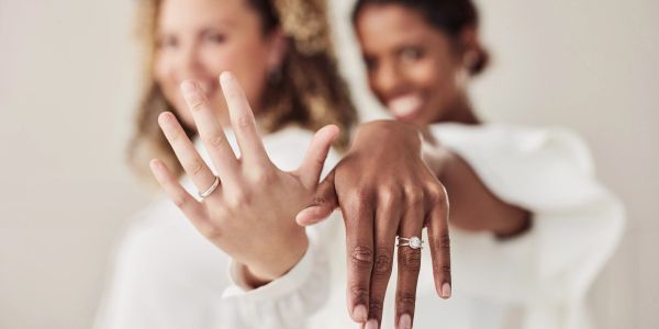 Two women displaying engagement rings on their hands.