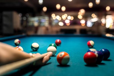 Image of a person playing billiards, aiming a pool cue at the cue ball on a pool table. 