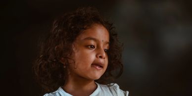 Portrait of a young girl with curly hair wearing a light blue shirt.