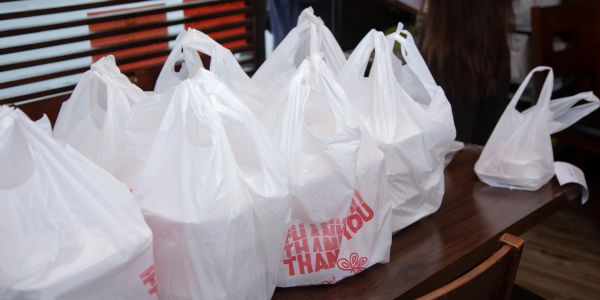 Multiple white plastic takeout bags on a wooden table.