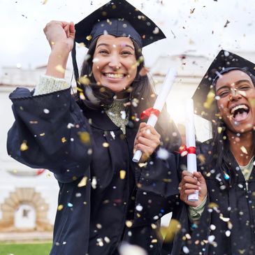 Two joyful graduates celebrating with diplomas and confetti outdoors.