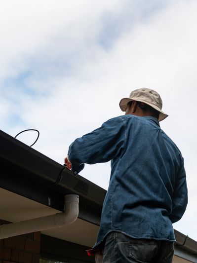 Man fixing gutters on a roof under a cloudy sky.