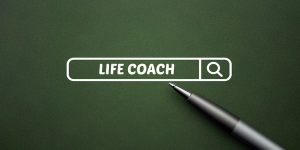 Pen pointing to a search bar with the words 'LIFE COACH' on a textured green background.