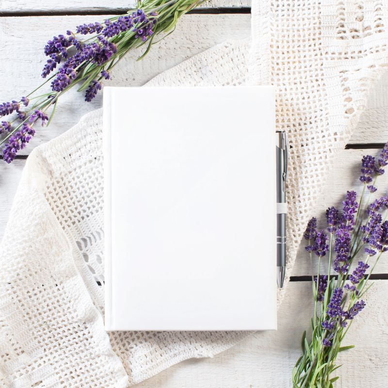 Blank white book with lavender flower frame on white lace and rustick wooden plank. Vintage style.