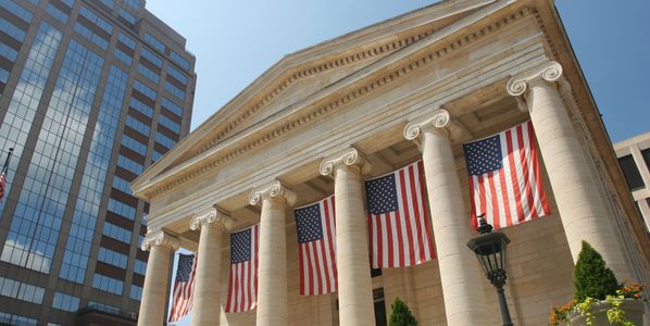 Historic building with American flags hanging from tall columns under a clear sky.
