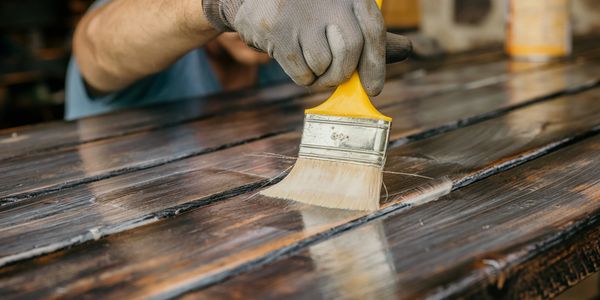 Person applying varnish on wooden surface with a paintbrush.