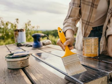 Person applying dark stain to wooden surface with a paintbrush outdoors.
