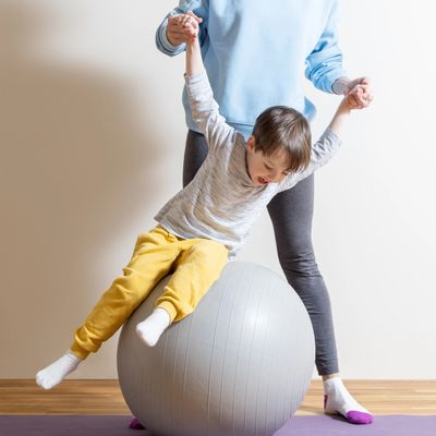 Child playing on exercise ball with adult assistance indoors.