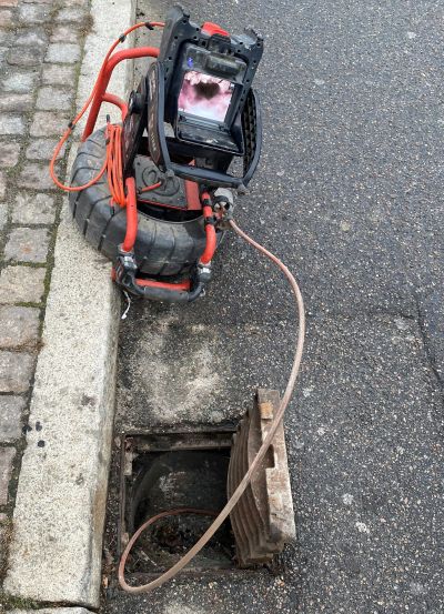 A sewer inspection camera setup near an open manhole on the street.