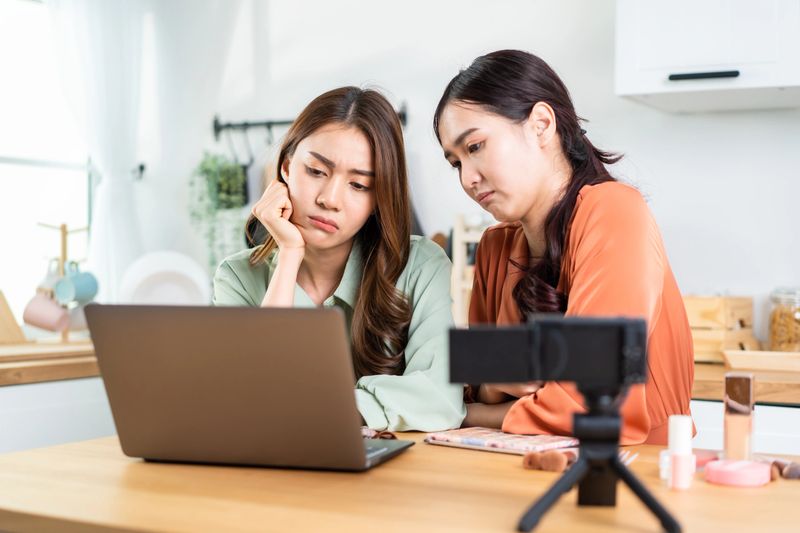 Asian Beauty blogger Influencer woman checking sale order on computer. Attractive beautiful business lesbian friend vlogger sit on table, using laptop computer to look at financial problem in house.