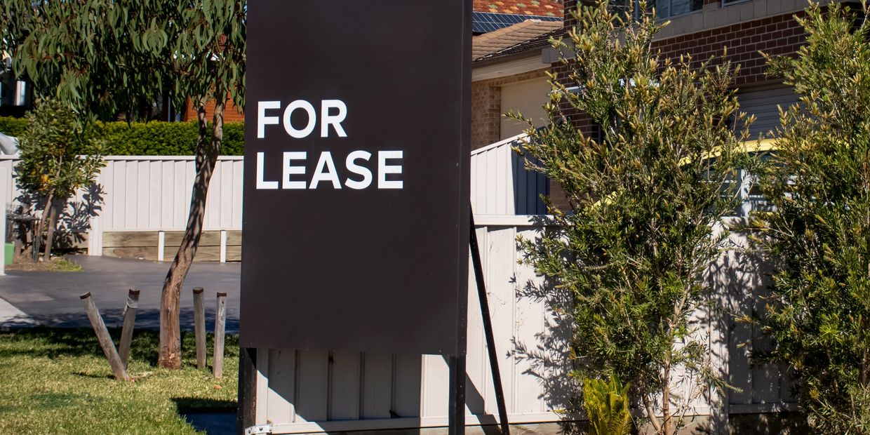 A black sign with white text saying "For Lease" in front of a house.