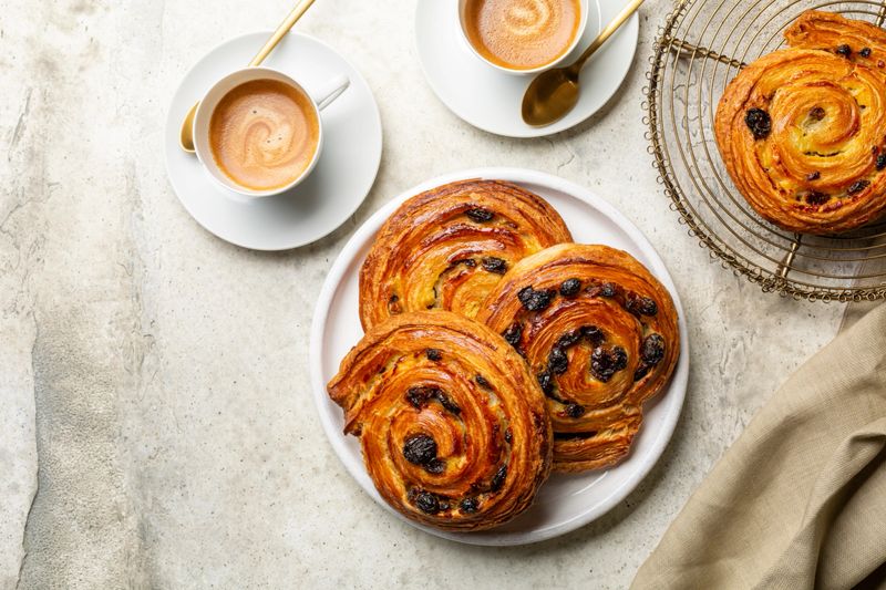 A selection of freshly baked French pastries on a pink plate, showcasing croissants, éclairs, and macarons.