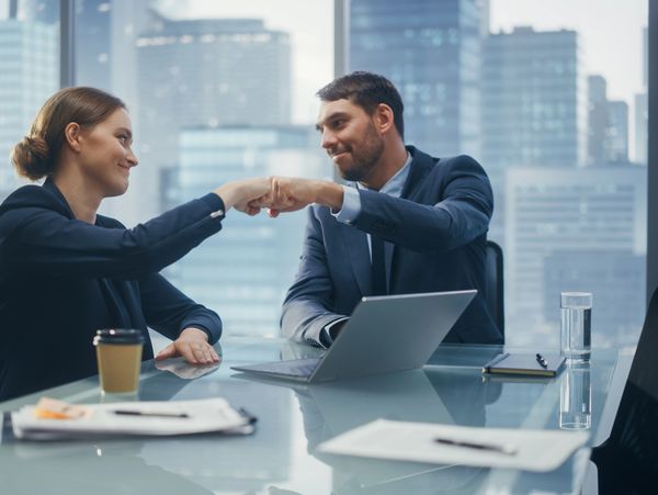 Two business professionals exchanging a fist bump in a modern office.