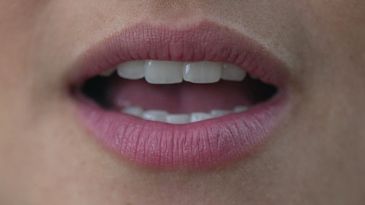 Close-up of a person's mouth speaking with natural pink lips and visible teeth.