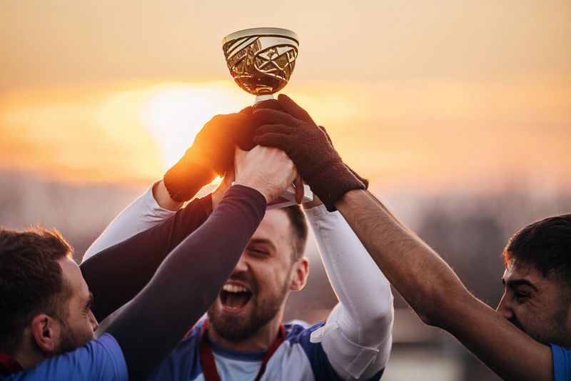Group of people, male soccer players celebrating because they won a trophy, on a soccer field on winter day outdoors.