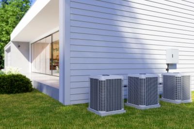 Three air conditioning units outside a modern house with white siding.