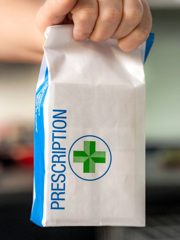 Hand holding a white prescription bag with a green cross symbol.