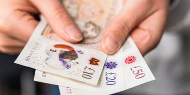 Hands holding various British pound banknotes including £10, £20, and £50.