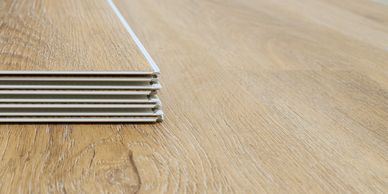 Stack of wooden laminate flooring planks on a wooden floor.
