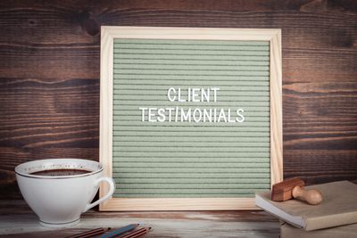 A cup of coffee on a desk with a notice saying client testimonials on a green background 