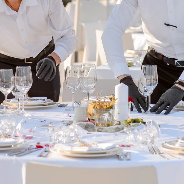 Waitstaff in white shirts and black gloves setting an elegant dining table.