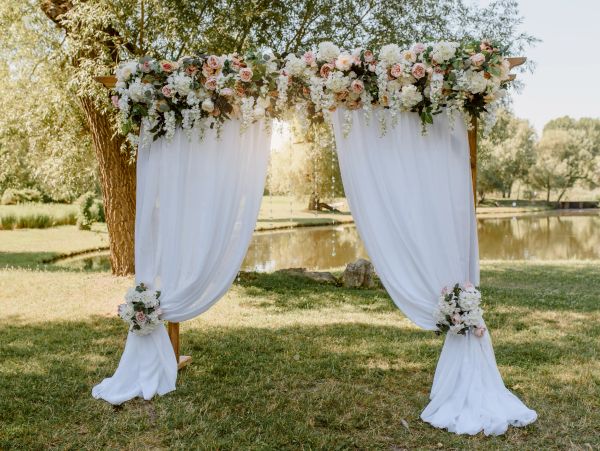 Floral wedding arch with white drapes outdoors.
