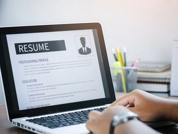 Person editing a resume on a laptop keyboard at a desk with stationery.