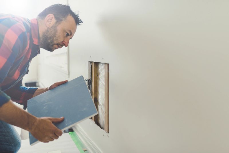 Man repairing the wall. He is holding a square piece of sheetrock ready to cover the hole in the wall